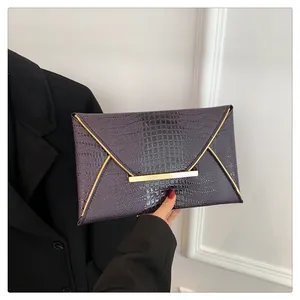 Detailed view of the dark purple crocodile texture and gold metal trim on the envelope bag