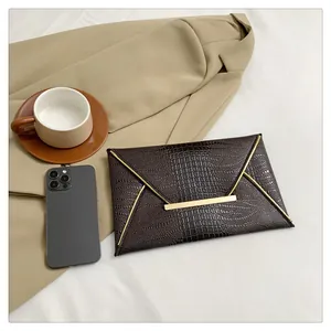 Detailed view of brown crocodile-pattern envelope clutch with gold metal trim in lifestyle scene