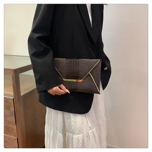 Detail of dark brown crocodile pattern envelope clutch with gold metal hardware accents