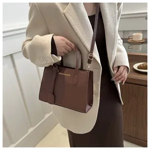 Brown square leather handbag with gold lettering and adjustable strap for urban commute