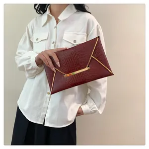 Detail of dark red crocodile pattern envelope clutch with gold metal trim held by model