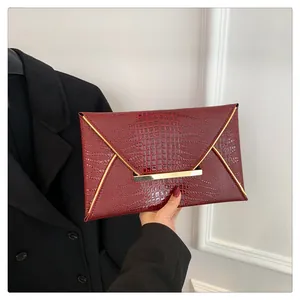 Close-up of burgundy envelope clutch bag with crocodile texture and gold V-shaped metal trim