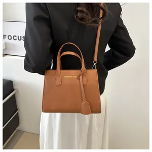 Brown leather crossbody bag with dual handles and gold lettering shown on a model