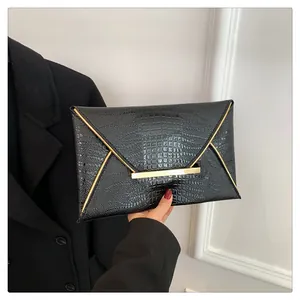 Detail of a black faux crocodile skin envelope clutch bag with gold metal trim in hand