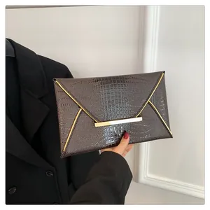Detail of dark brown croc-embossed envelope clutch with gold metal trim and clasp