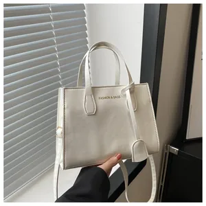 Close-up of beige square tote bag with FASHION & BAGS text and golden hardware