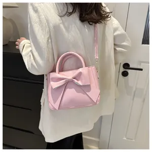 Pale pink small square handbag with large bow detail shown on a model in a room