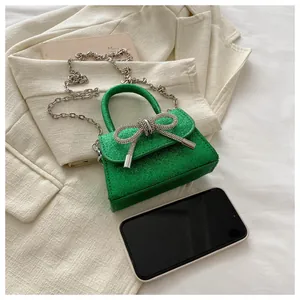 Détail du mini sac à paillettes vertes avec nœud en strass sur blazer beige