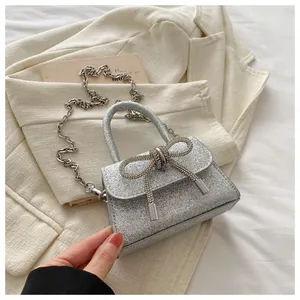 Détail d'un mini sac à main pailleté argenté avec un grand nœud en cristal et bandoulière