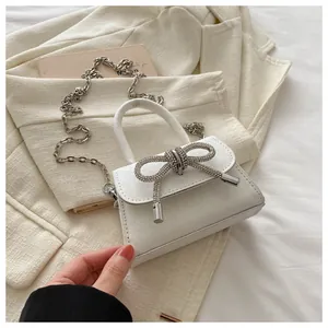 Détail d'un mini sac blanc pailleté avec un nœud en strass argentés et une bandoulière chaîne