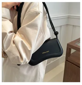 Detailed view of black leather underarm bag featuring gold Miss mini text and knotted strap