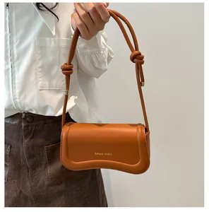 Detail showing the wavy bottom design and knot strap on a caramel mini shoulder bag