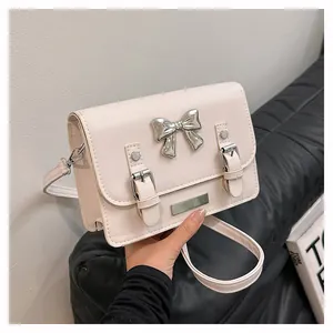 Detail of a creamy white PU leather square crossbody bag with a silver bow and belt straps
