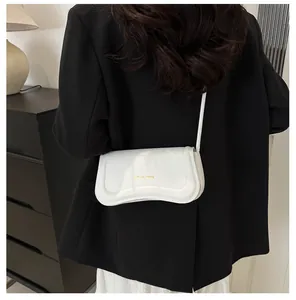 Close-up of white glossy leather shoulder bag with gold logo and long strap