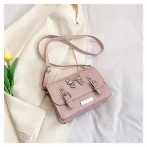 Close-up of pink crossbody bag with silver metal bow and decorative straps on white fabric