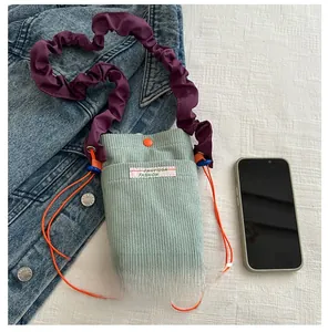 Detail of green corduroy phone bag with purple pleated strap and orange drawstring