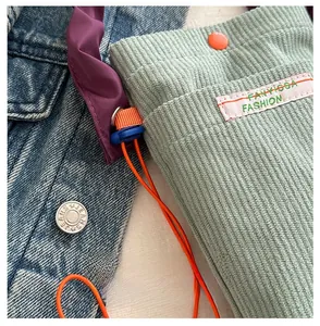 Detail of light green corduroy mini bag with orange strap and woven fashion label