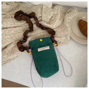 Detail of green corduroy crossbody bag with brown ruched strap and yellow button accent