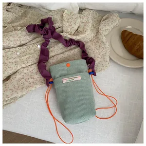 Detail view of mint green corduroy phone bag with purple ruffled strap and orange accents