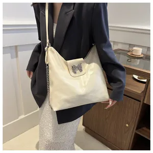 Gros plan d'un sac hobo blanc crème avec fermoir nœud argenté et bandoulière en cuir chaîne