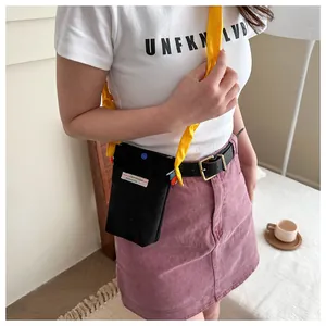 Detail of black corduroy phone bag with contrasting yellow strap and decorative label