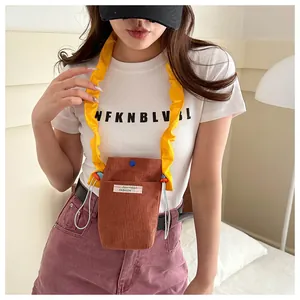 Detail of brown corduroy crossbody phone bag featuring yellow ruffled strap and blue snap