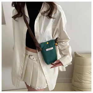 Green corduroy crossbody phone bag with contrast drawstrings worn by a model in nature