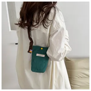 Detailed view of green corduroy crossbody phone bag with yellow button and strap on a model