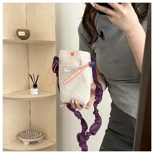 Detail view of corduroy phone bag featuring purple pleated strap and orange drawstring accents