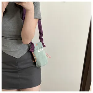 Close-up of light green corduroy crossbody bag with purple pleated strap and orange drawstring