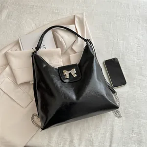 Sac cabas noir tendance avec nœud argenté posé sur un costume beige et un magazine
