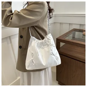 Detail of white drawstring shoulder bag with bow decor and silver metal chain strap