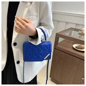 Mini sac carré matelassé bleu porté par un mannequin en blazer blanc dans un décor minimaliste