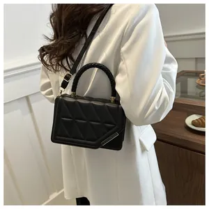 Détail du sac matelassé noir avec poignée tressée porté sur un blazer blanc