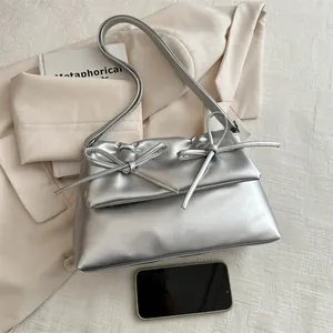 Silver metallic underarm bag with bows and long strap shown with smartphone for scale
