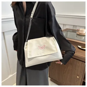 Détail de broderie papillon rose sur sac bandoulière en toile crème avec chaîne argent