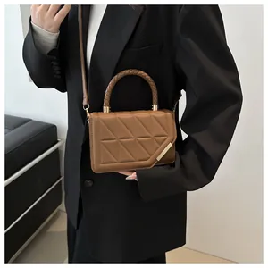 Sac bandoulière marron matelassé avec poignée tressée porté sur un blazer noir chic