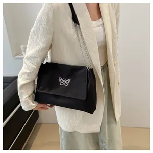 Détail de broderie papillon et bandoulière chaîne argentée sur un sac sous le bras