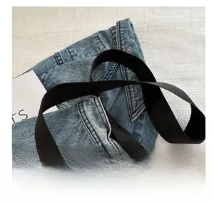 Close-up of wide black fabric strap on washed blue denim crossbody bag texture