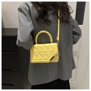 Détail d'un sac à bandoulière matelassé jaune vif avec poignée tressée sur costume