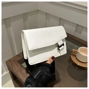 Close-up of a white square crossbody bag with a wide black shoulder strap and buckle