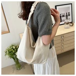 Détail du sac Hobo en toile blanche avec bandoulière à volants plissés porté par un mannequin