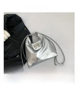 Detail of silver metallic shoulder bag featuring a decorative metal bow and slim strap