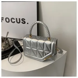 Détail d'un petit sac argenté matelassé avec poignée tressée et finitions métalliques dorées