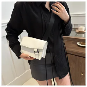 White minimalist square flap bag with black wide strap shown on a model in a cafe setting
