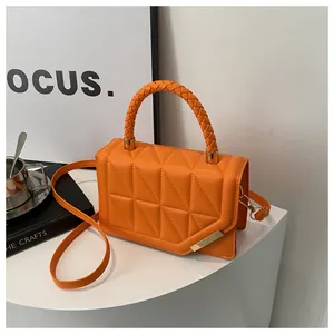 Détail du sac à main orange matelassé avec poignée tressée et finitions dorées chic