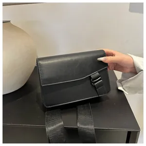 Detail of minimalist black square PU bag with flap closure and wide nylon shoulder strap