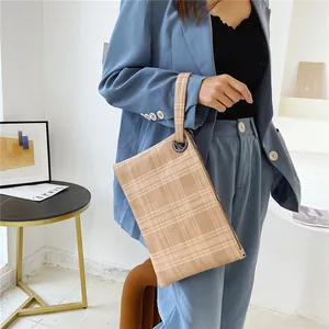 Pochette a busta a quadri beige con cinturino da polso tenuta da una modella in tailleur