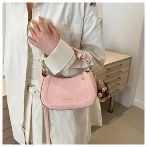Detail of pink shoulder bag with knot handle, gold logo, and furry monster charm accessory