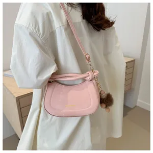 Detail of pink faux leather half-moon bag featuring gold logo and brown pom-pom charm